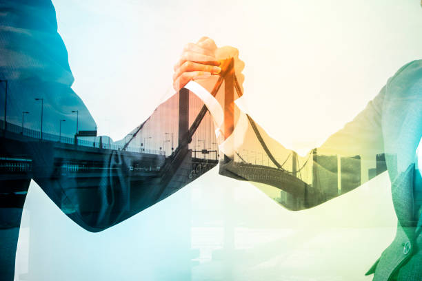 Double exposure of two clasped hands over a bridge and city skyline, representing a strong customer partnership